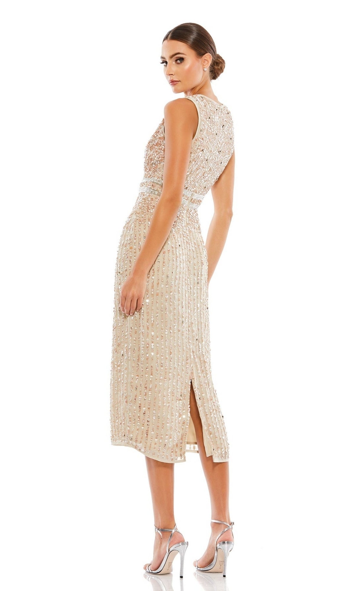 A woman stands against a white background wearing the Mac Duggal 10509 short sequin wedding guest dress—sleeveless, knee-length, beige, with a back slit—paired with silver high-heeled sandals.